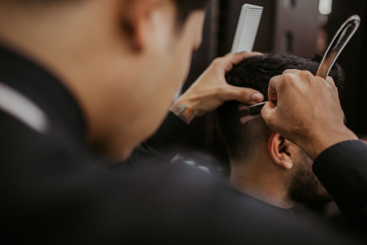 Close-up of a barber expertly styling a mans hair with a razor and comb in a trendy barbershop.